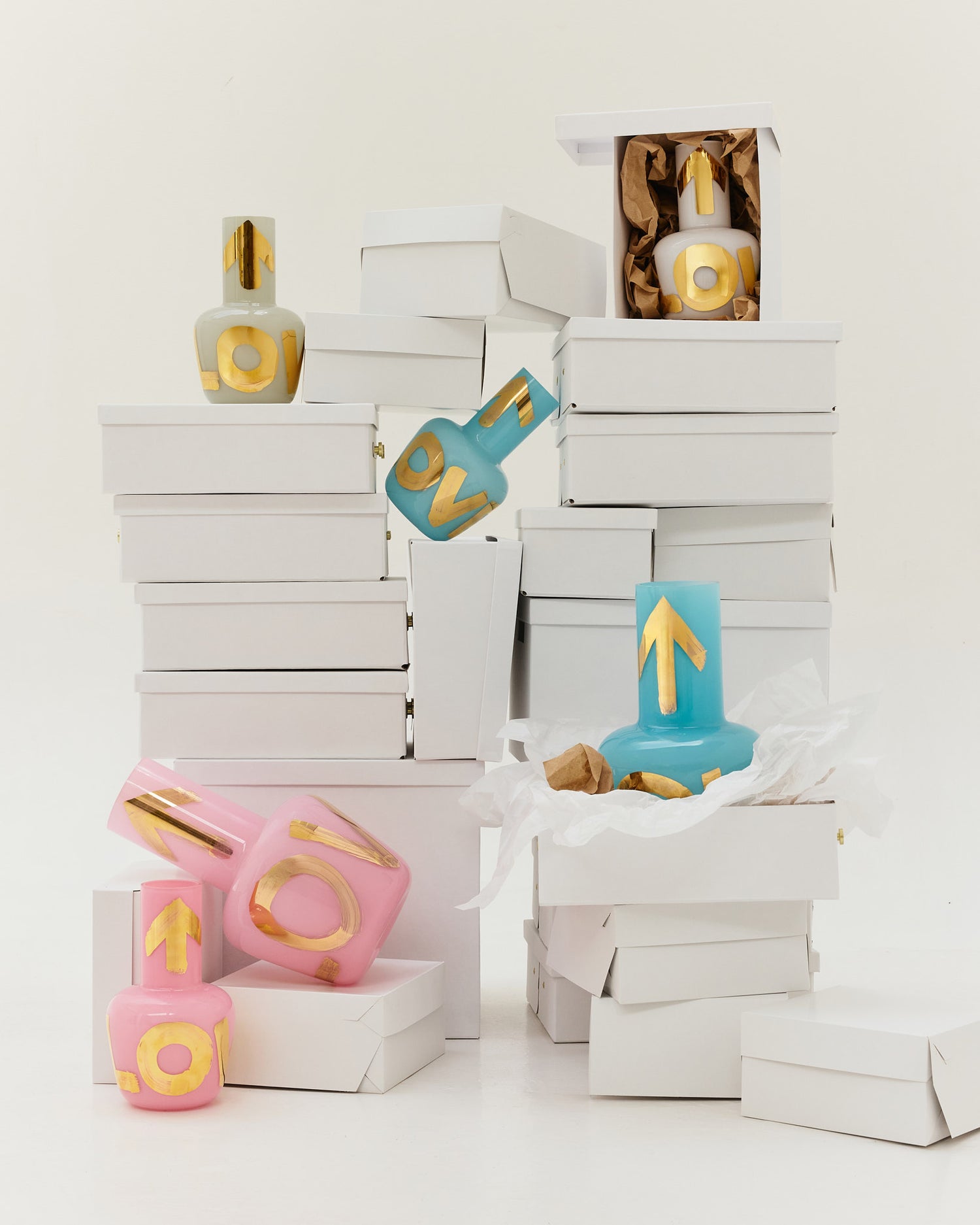 Colorful decorative candles with gold accents in various shapes surrounded by white packaging boxes.