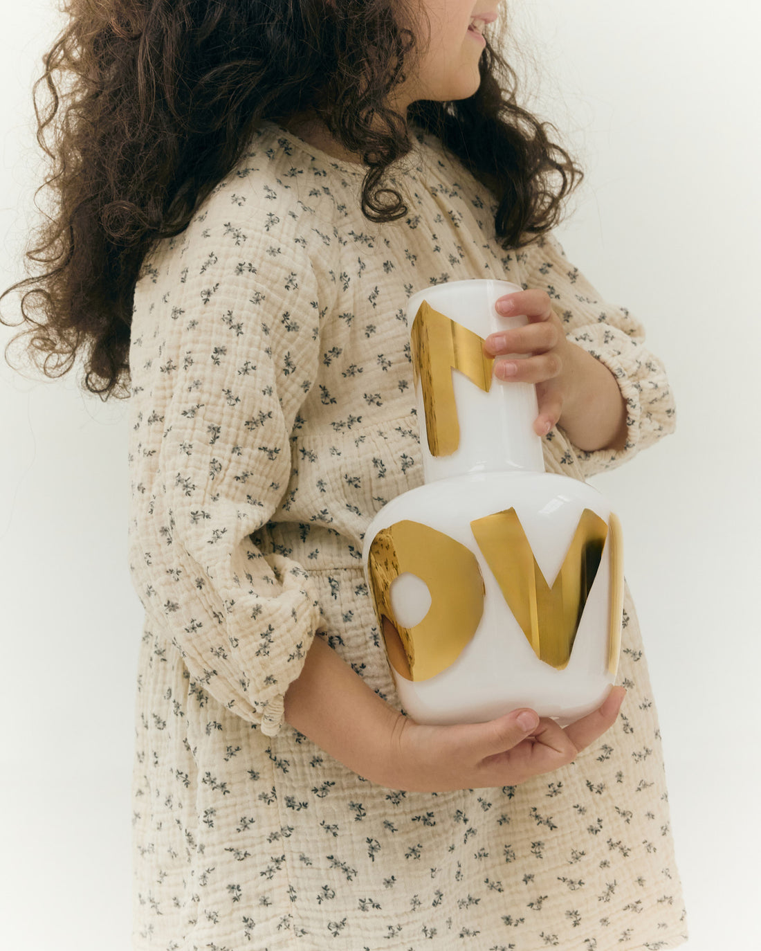 Dívka držící bílou vázu Unnamed s nápisem LOVE v pravém zlatě, součást exkluzivní kolekce Artisème x QUBUS.